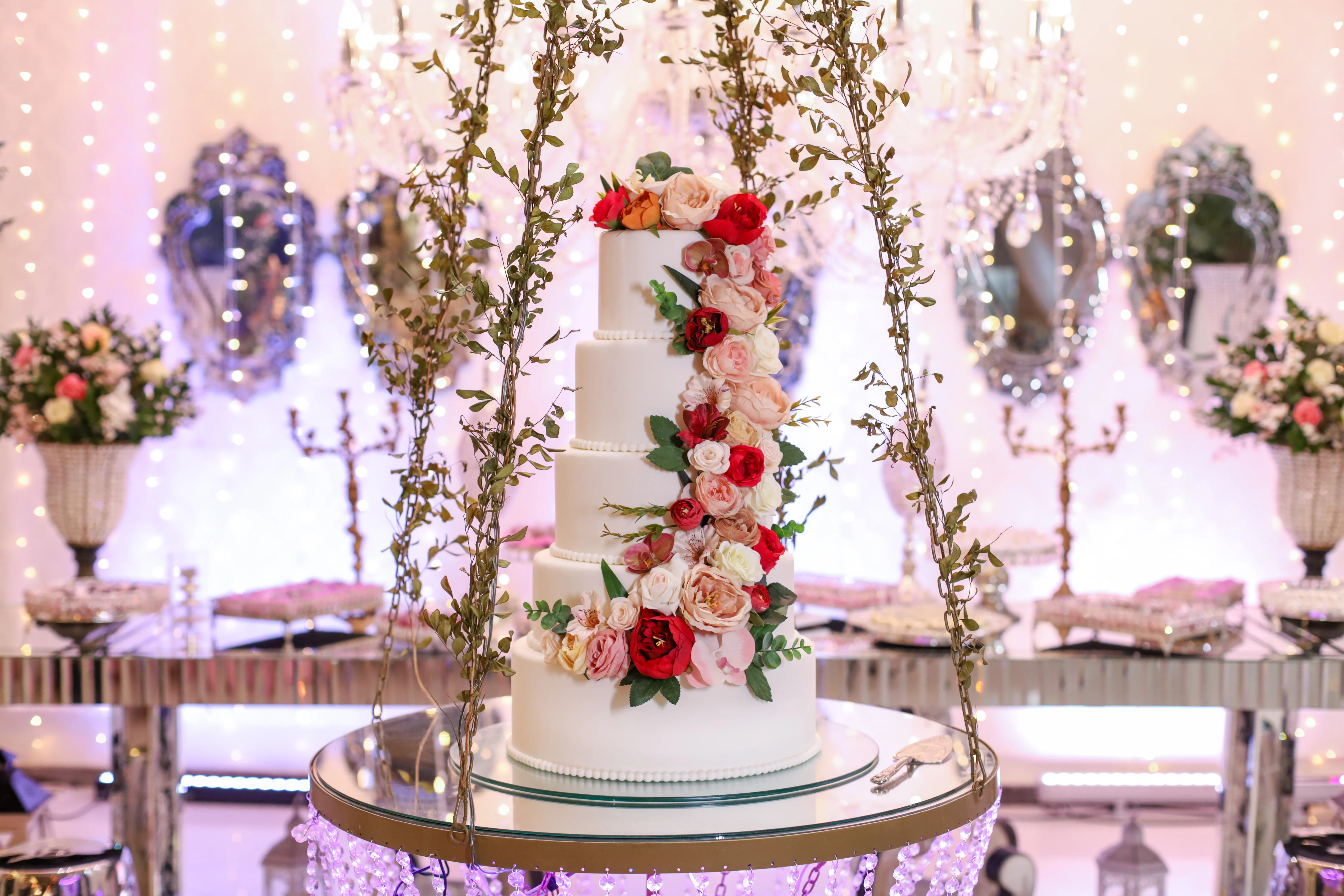 Mesa do bolo majestosa com cascata floral e doces finos sob os lustres de cristal do Espaço Luz