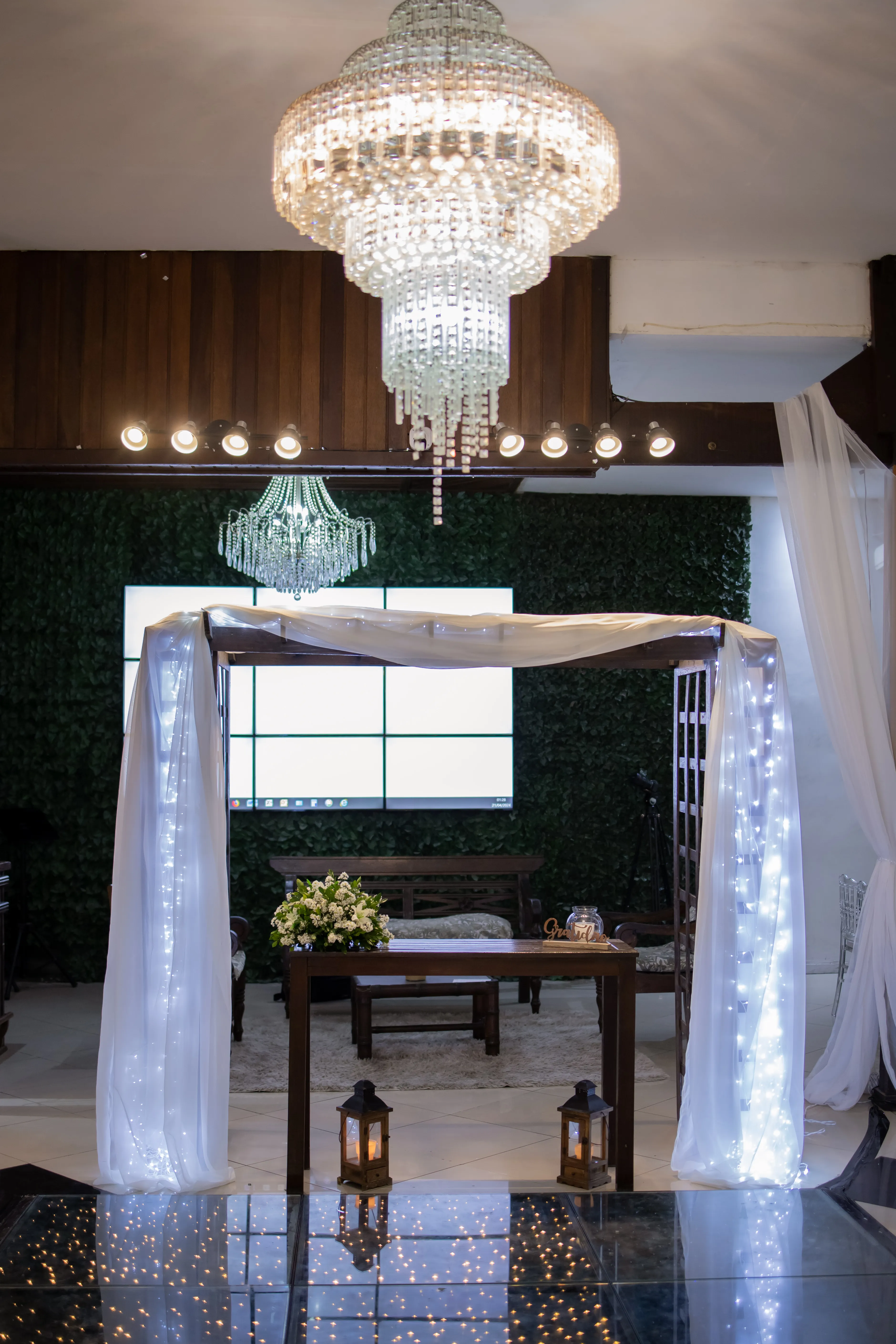 Pergolado de madeira com tecidos fluidos e iluminação cênica no Jardim Encantado para cerimônia de casamento