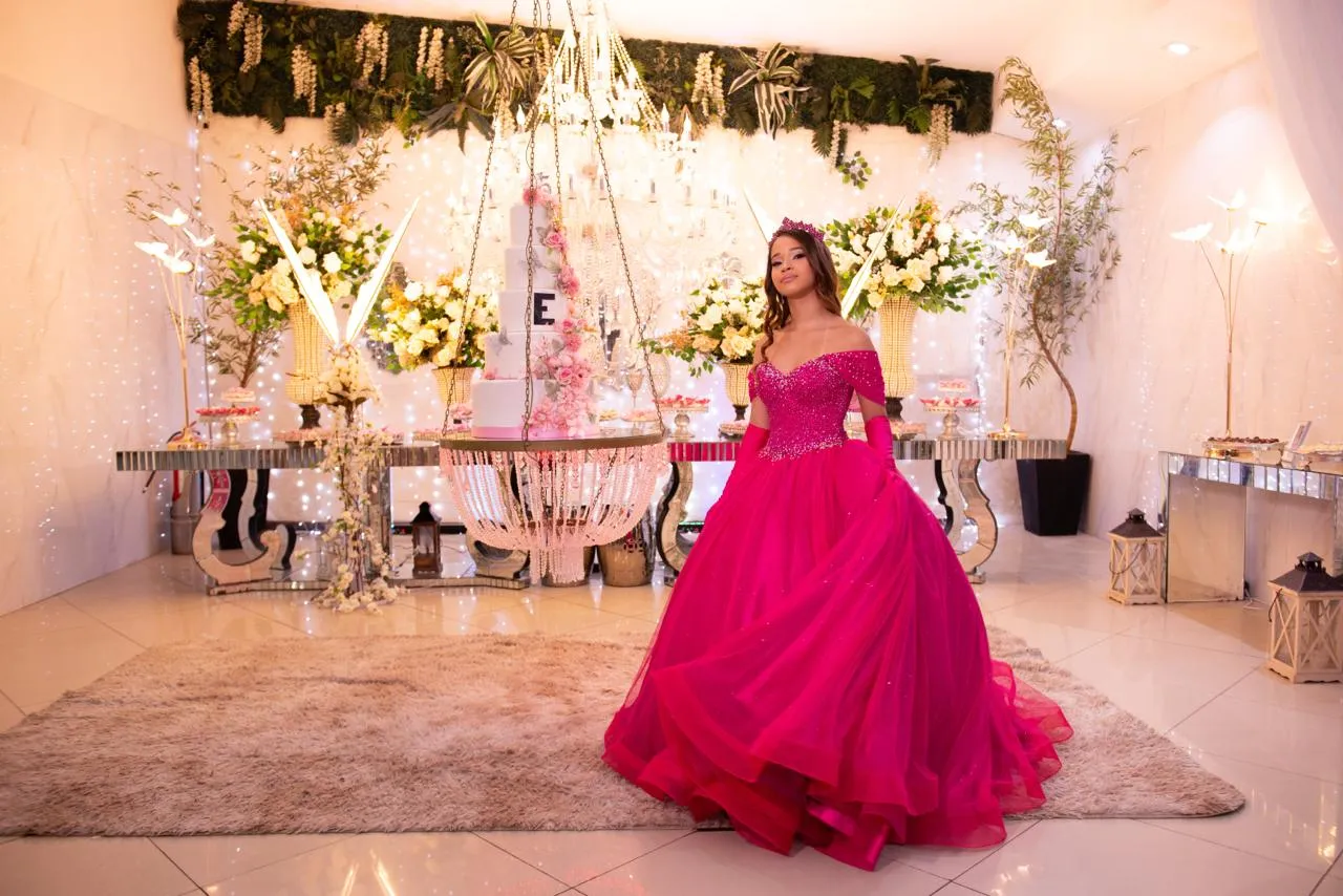 Debutante Eloisa com vestido rosa clássico sob o brilho do lustre de cristal na mesa de doces do Espaço Luz
